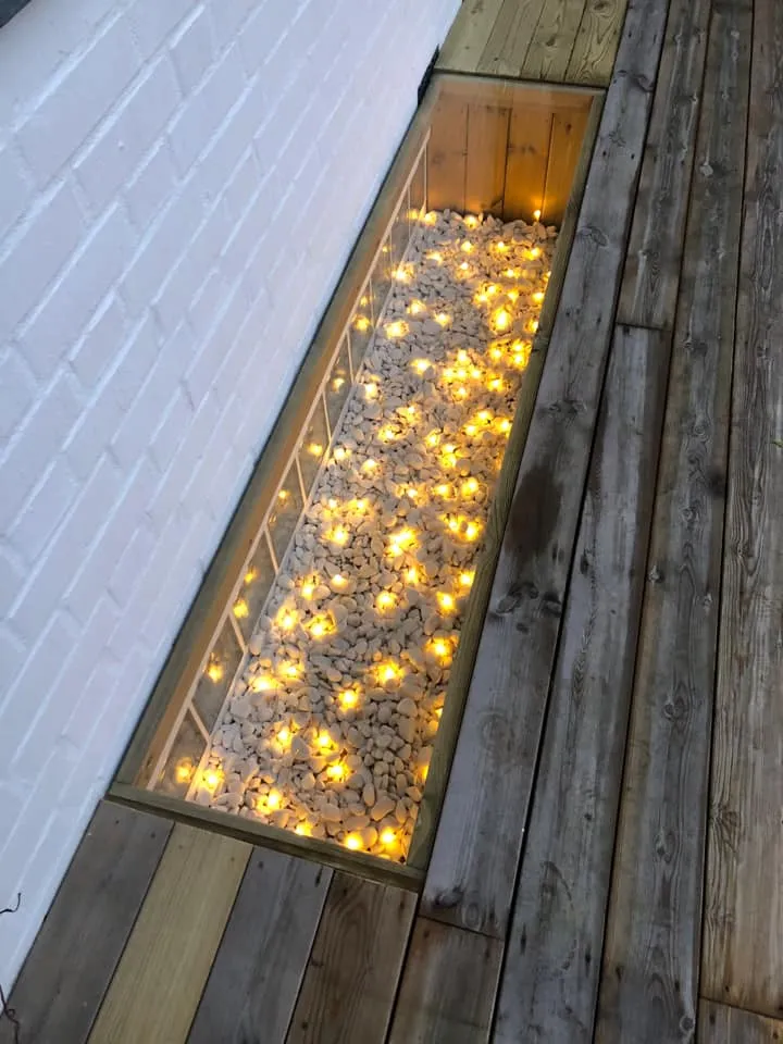 Ljusgård täckt med glas, vita stenar och LED-belysning som lyser varmvitt