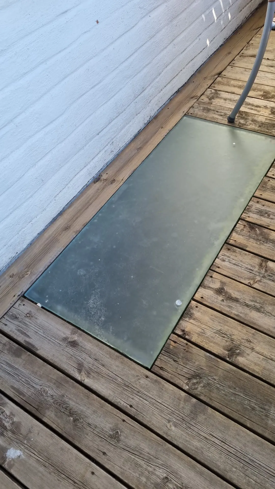 Flat glasskiva lagd över källarfönster i altandäcket