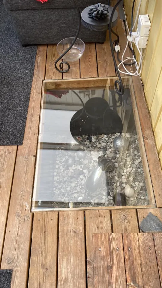 Glasskiva över ljusgård med dekorativa stenar och trädgårdsdekoration