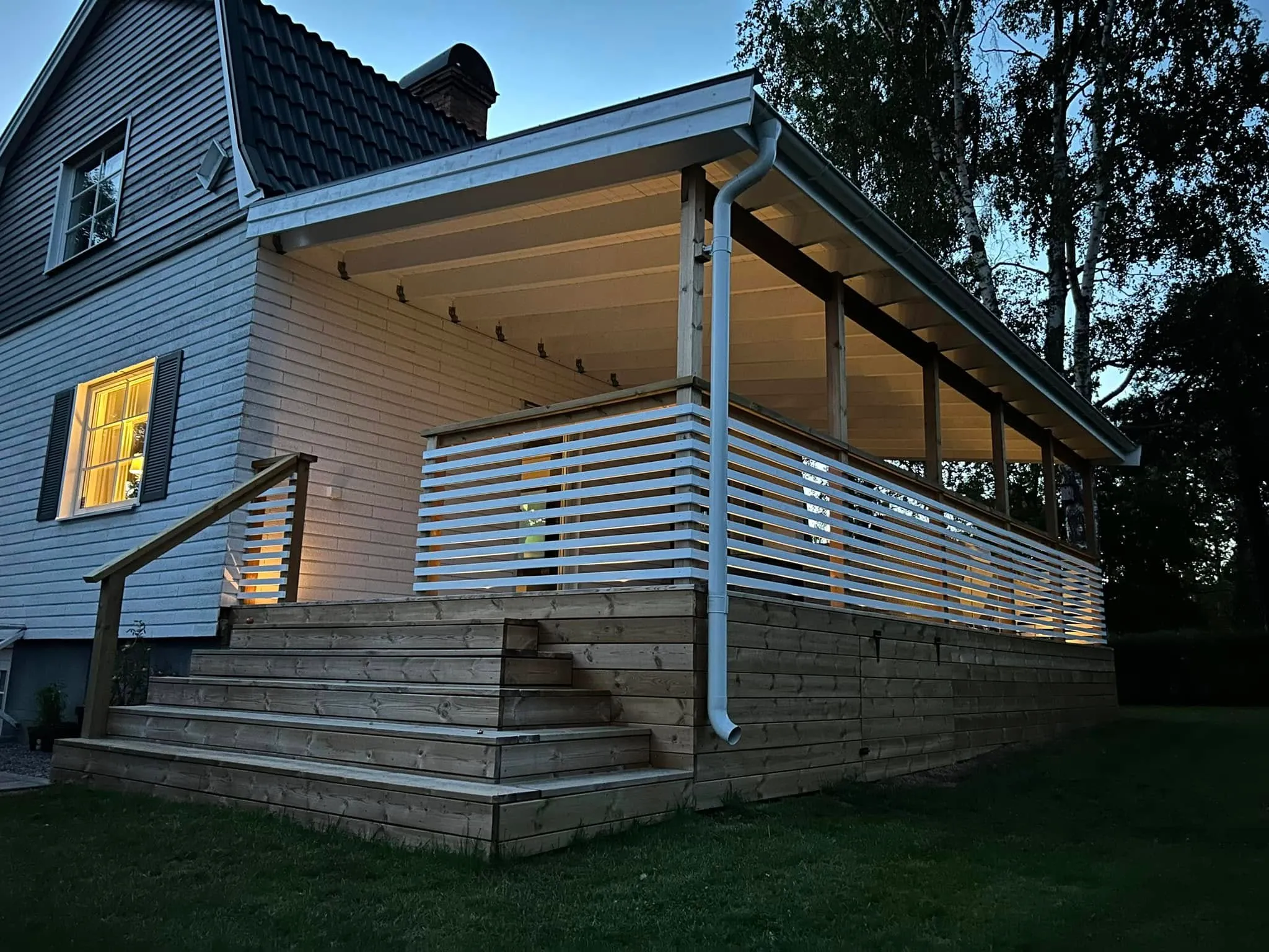 Närbild på altanens sida med tak, trappa, vitmålat räcke och LED-belysning