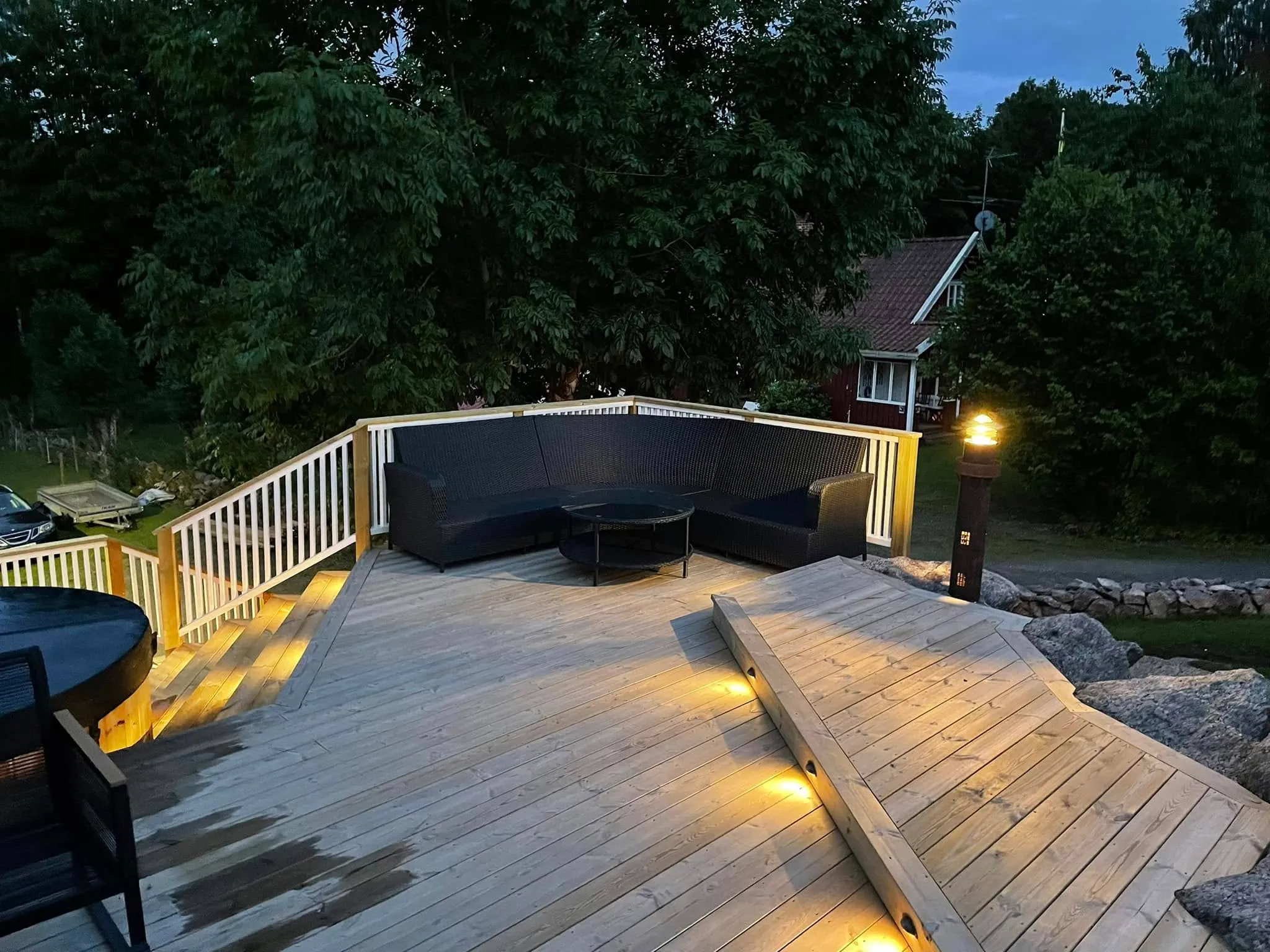 Flernivåaltan på berghäll i skymning med utesoffa och infälld LED-trappbelysning