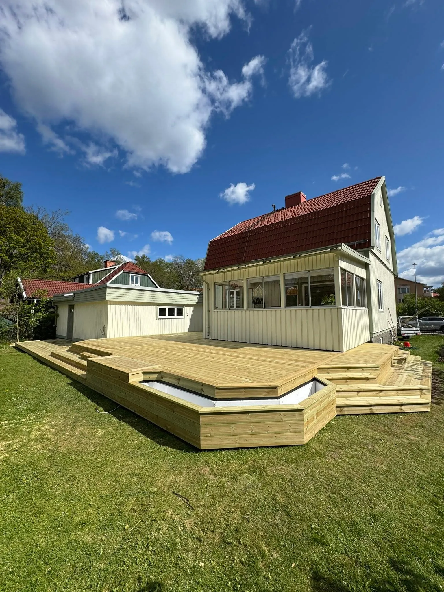 Låg altan med brutet hörn och integrerat planteringskärl i ljust trä