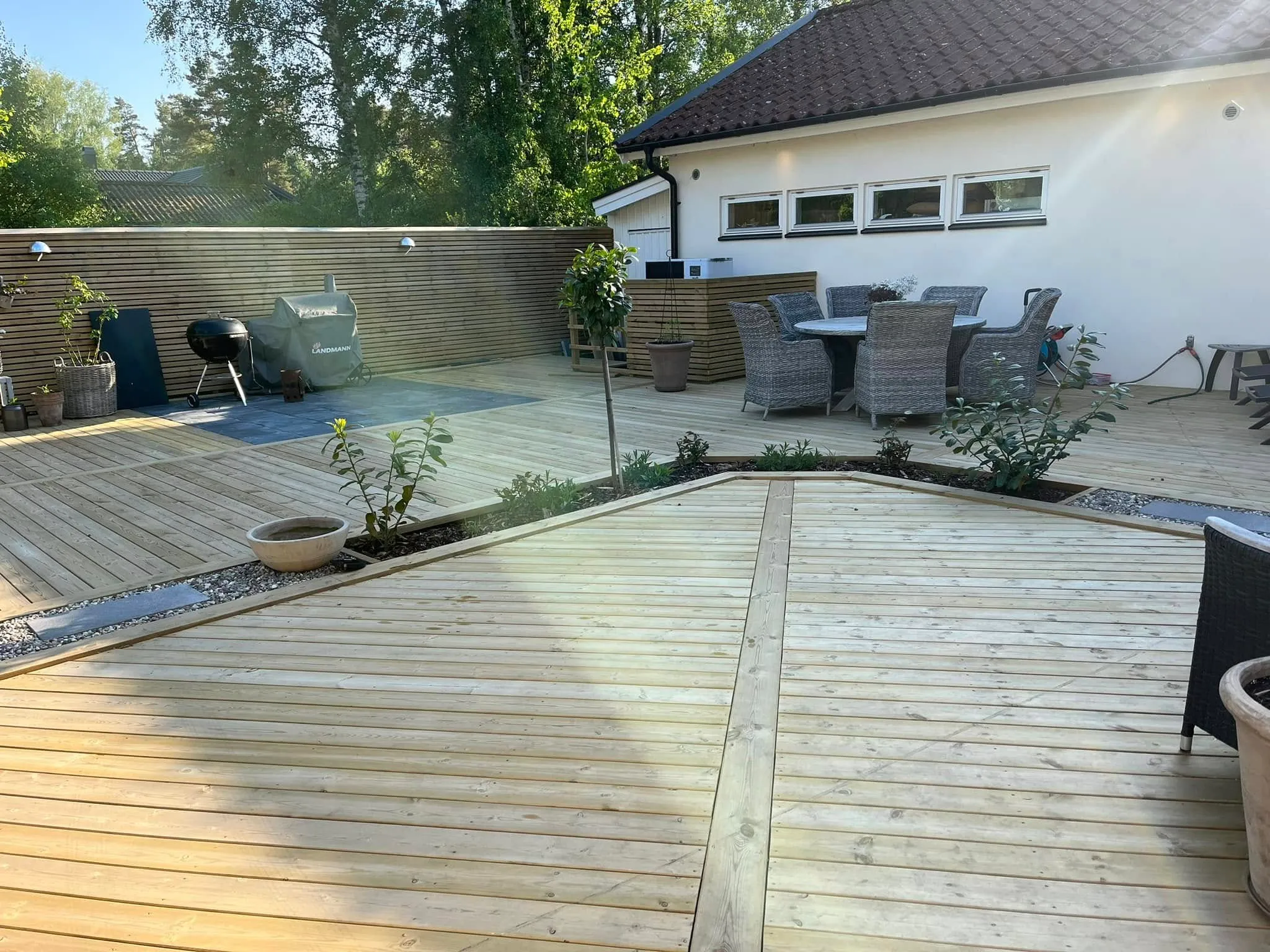 Altan med utemöbler, grill och vit pergola intill planteringslådor