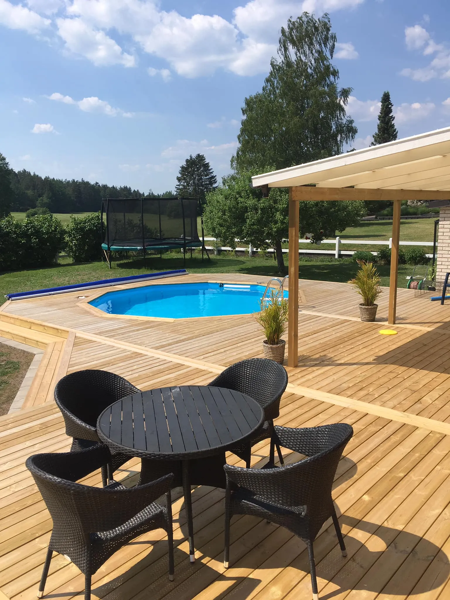 Poolaltan i ljust trä med rund pool och skyddad loungedel under tak