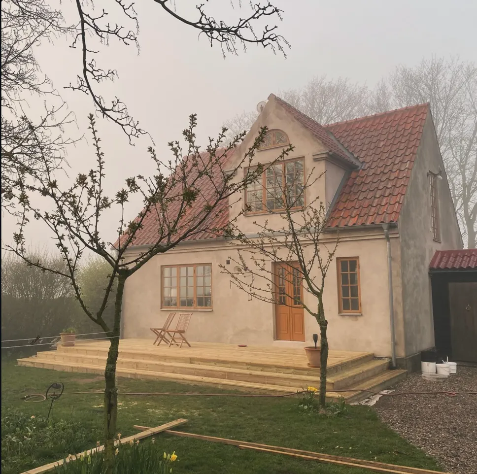 Stefans färdigbyggda altan sedd från trädgården — trappsteg runt putsat hus