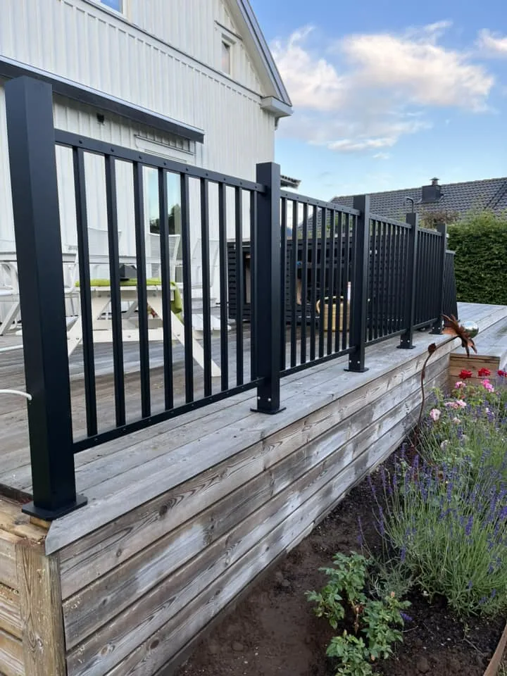 Svart metallräcke med stående ribbor och överliggare, monterat på en altan.