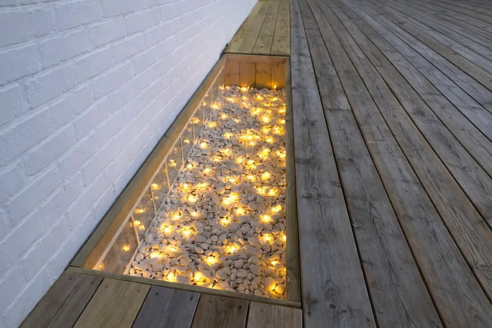 Ljusgård under altan med glas, vita stenar och LED-belysning